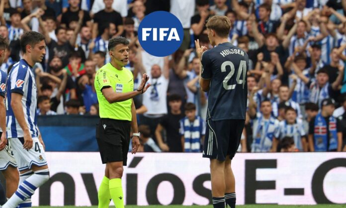 Gil Manzano hablando con Dean Huijsen y el logo de la FIFA. 